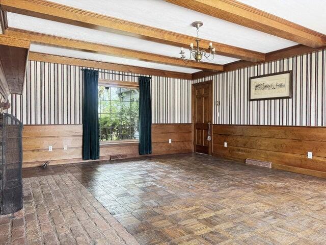 unfurnished room featuring wooden walls, beamed ceiling, a chandelier, and visible vents