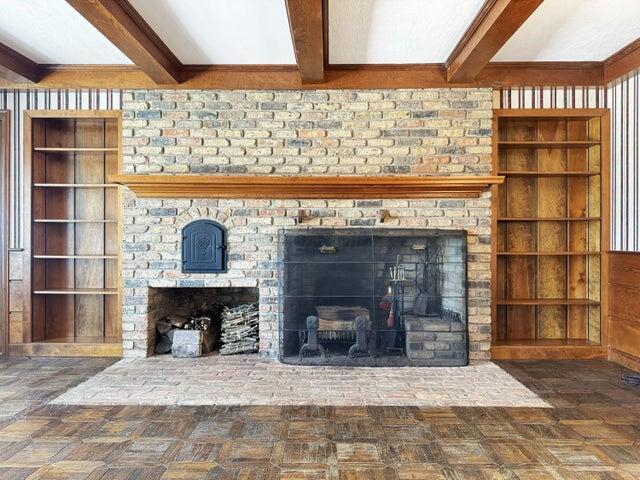interior details featuring beamed ceiling, a brick fireplace, and built in shelves