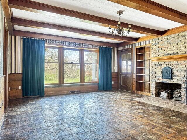 unfurnished living room featuring a chandelier, built in features, beam ceiling, and plenty of natural light