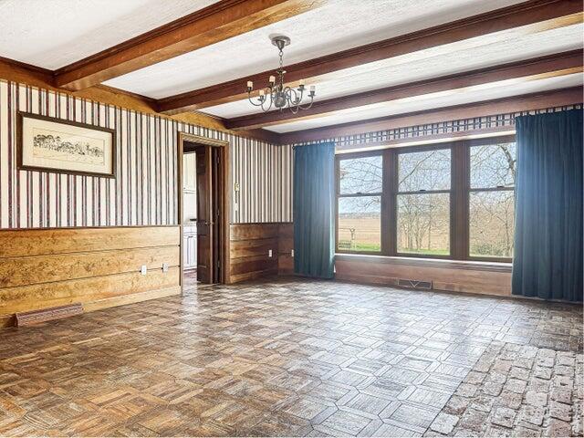 spare room featuring baseboards, beam ceiling, and a chandelier