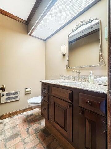 half bathroom with vanity, baseboards, toilet, heating unit, and ornamental molding