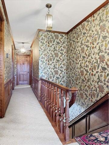 hallway with crown molding, wallpapered walls, an inviting chandelier, and light carpet