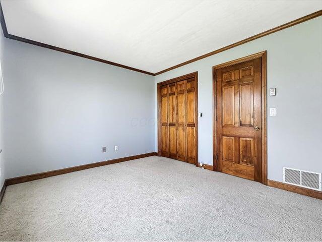 unfurnished bedroom with light colored carpet, baseboards, visible vents, and ornamental molding