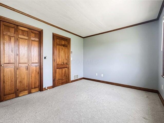 unfurnished bedroom with light colored carpet, visible vents, baseboards, a closet, and ornamental molding