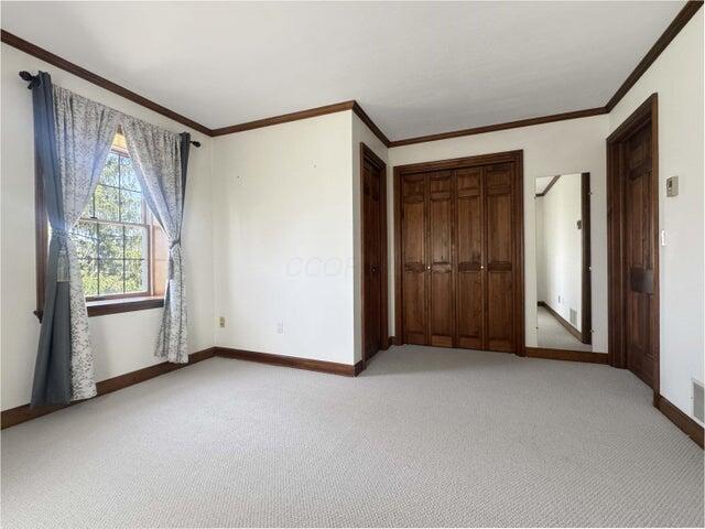 unfurnished bedroom featuring crown molding, baseboards, a closet, and light carpet