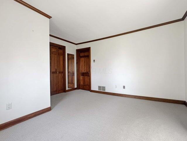 spare room with crown molding, baseboards, light colored carpet, and visible vents
