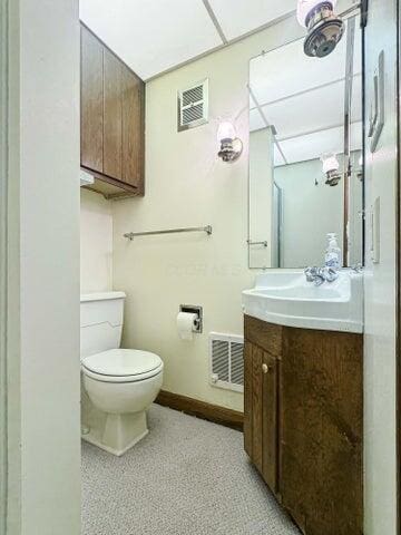 half bath with visible vents, baseboards, toilet, and vanity
