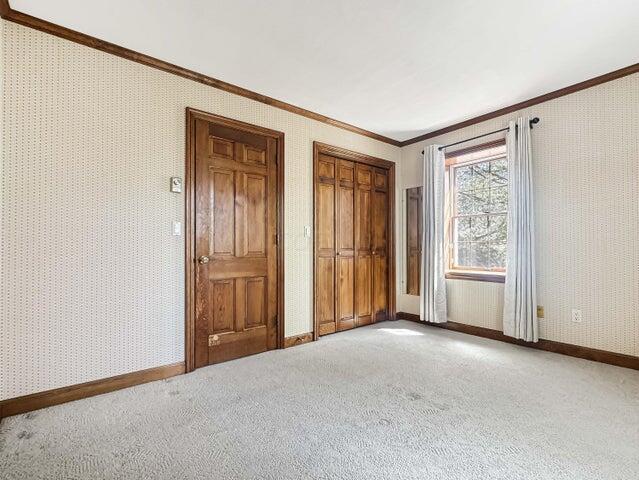 unfurnished bedroom featuring wallpapered walls, ornamental molding, and light carpet