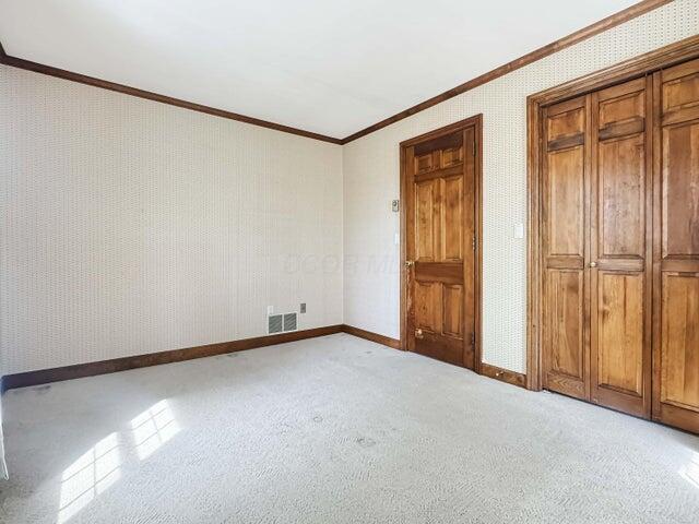 unfurnished bedroom featuring light colored carpet, crown molding, visible vents, baseboards, and wallpapered walls