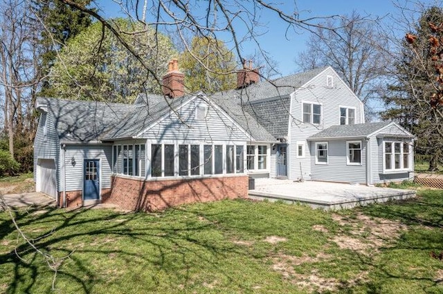 rear view of house featuring a chimney, a sunroom, a patio area, an attached garage, and a yard
