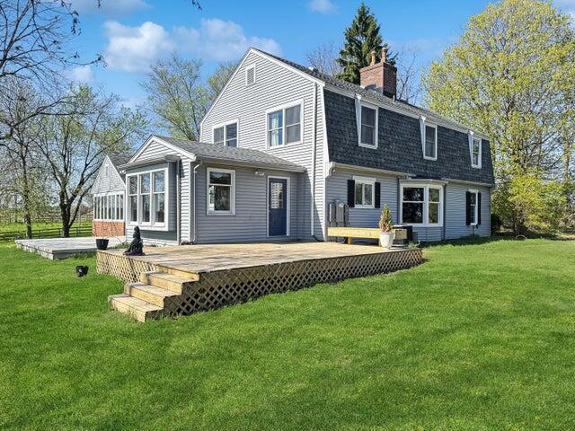 rear view of house featuring a chimney, roof with shingles, a lawn, a wooden deck, and a gambrel roof