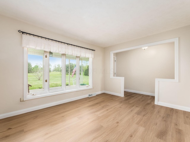 empty room with baseboards, visible vents, and light wood finished floors