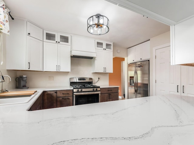 kitchen featuring a sink, appliances with stainless steel finishes, light stone countertops, and glass insert cabinets