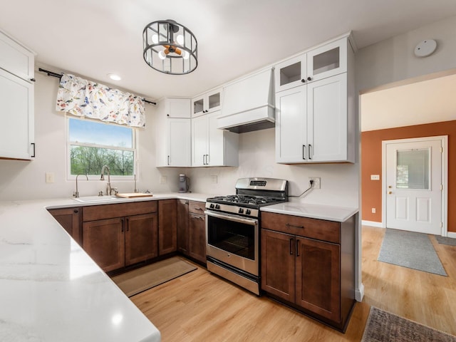 kitchen with gas range, light wood-type flooring, white cabinetry, custom range hood, and a sink