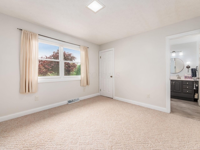 unfurnished bedroom featuring baseboards, light carpet, ensuite bath, and visible vents