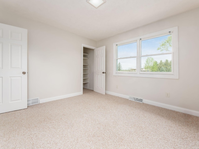 unfurnished bedroom featuring visible vents, carpet flooring, baseboards, and a walk in closet