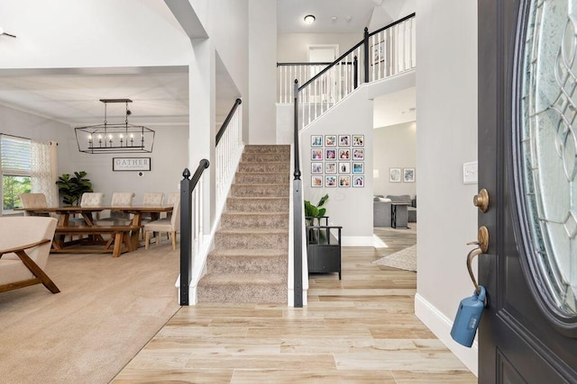 foyer entrance with baseboards, light wood-style floors, a notable chandelier, and stairway