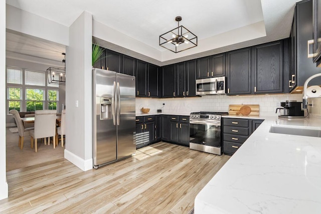 kitchen featuring an inviting chandelier, light stone countertops, light wood-style floors, a sink, and appliances with stainless steel finishes