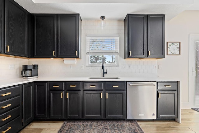 kitchen with stainless steel dishwasher, backsplash, a sink, and light wood-style flooring