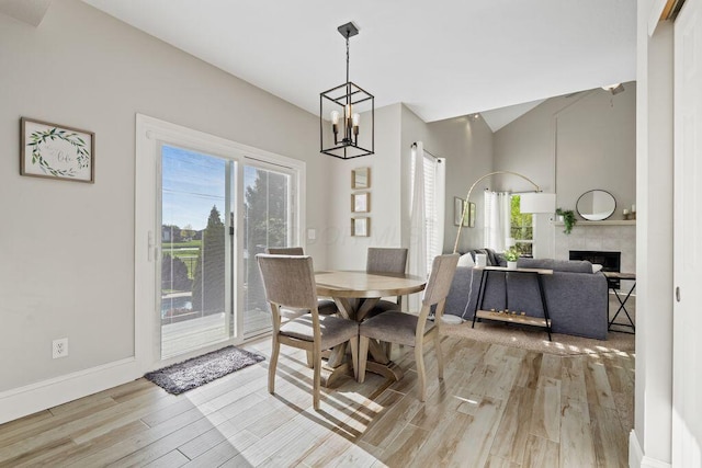 dining space featuring light wood-style floors, a chandelier, baseboards, a tile fireplace, and vaulted ceiling