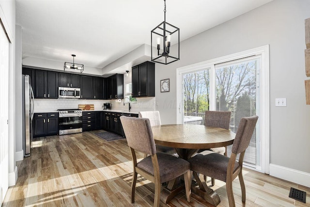 dining area with visible vents, light wood-style flooring, baseboards, and a notable chandelier