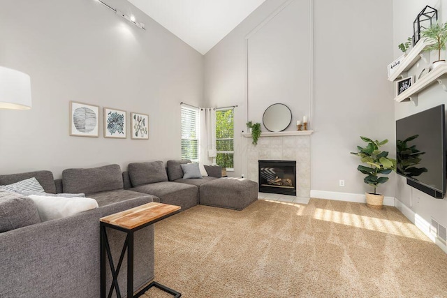 living area featuring carpet floors, high vaulted ceiling, rail lighting, baseboards, and a tile fireplace