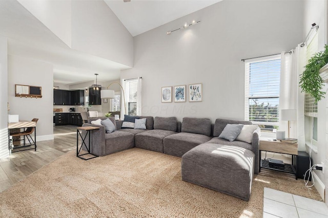 living area with high vaulted ceiling, baseboards, and light wood-style floors