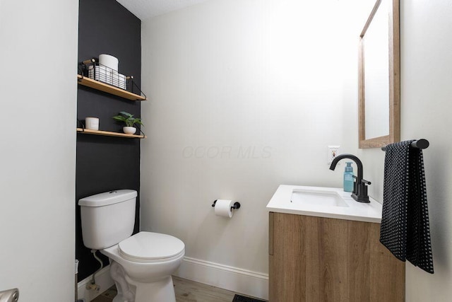 bathroom featuring baseboards, wood finished floors, toilet, and vanity