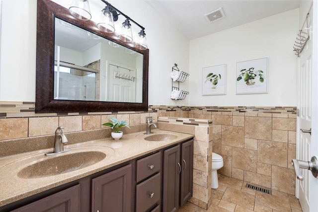 bathroom featuring visible vents, a sink, toilet, and tile walls
