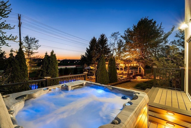 pool at dusk with a hot tub and a wooden deck
