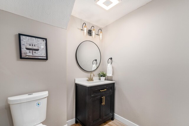 bathroom featuring baseboards, toilet, wood finished floors, and vanity