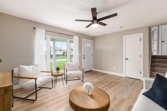 living room with ceiling fan, baseboards, light wood-style flooring, stairs, and a textured ceiling