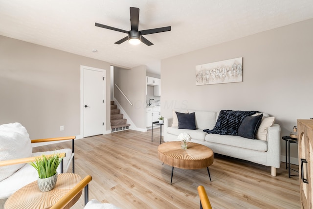 living area with stairway, a ceiling fan, light wood finished floors, and baseboards