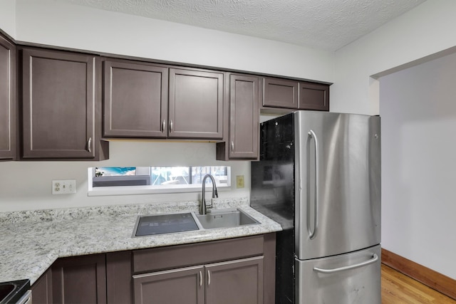 kitchen with electric range, dark brown cabinets, a sink, freestanding refrigerator, and light wood-style flooring