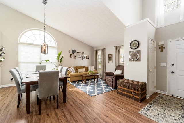 dining area with baseboards, wood finished floors, a notable chandelier, and high vaulted ceiling