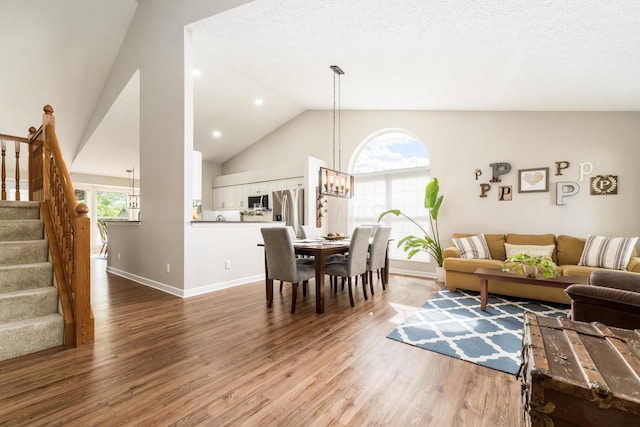 living room with stairway, a wealth of natural light, wood finished floors, and a chandelier