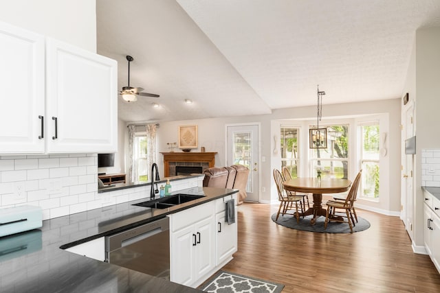 kitchen with stainless steel dishwasher, a ceiling fan, a fireplace, dark countertops, and a sink