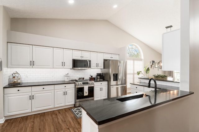 kitchen featuring dark countertops, a sink, a peninsula, lofted ceiling, and stainless steel appliances