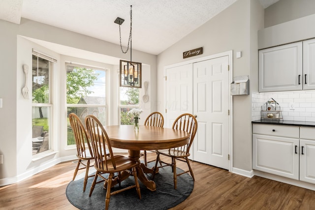 dining space featuring baseboards, a textured ceiling, light wood finished floors, and vaulted ceiling