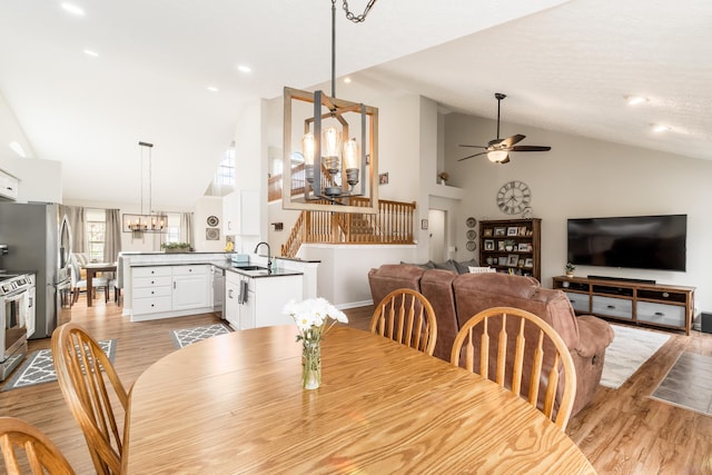 dining area featuring light wood-style floors, ceiling fan with notable chandelier, and high vaulted ceiling