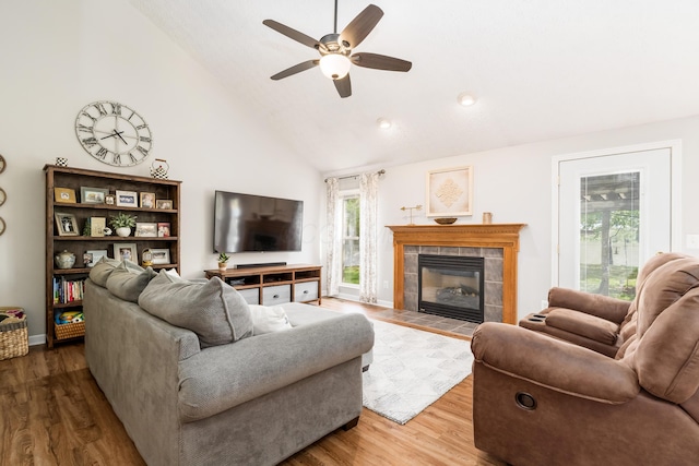 living area with a tiled fireplace, a ceiling fan, wood finished floors, and high vaulted ceiling
