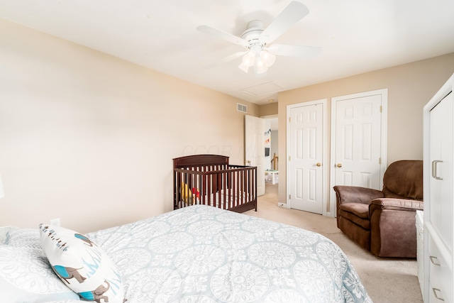 bedroom featuring a ceiling fan, attic access, visible vents, multiple closets, and light carpet