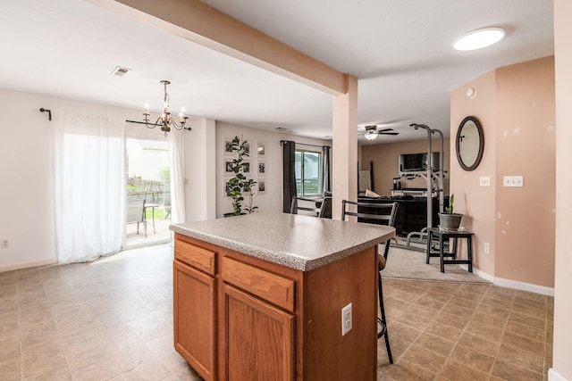 kitchen with brown cabinetry, ceiling fan with notable chandelier, a center island, baseboards, and a kitchen bar