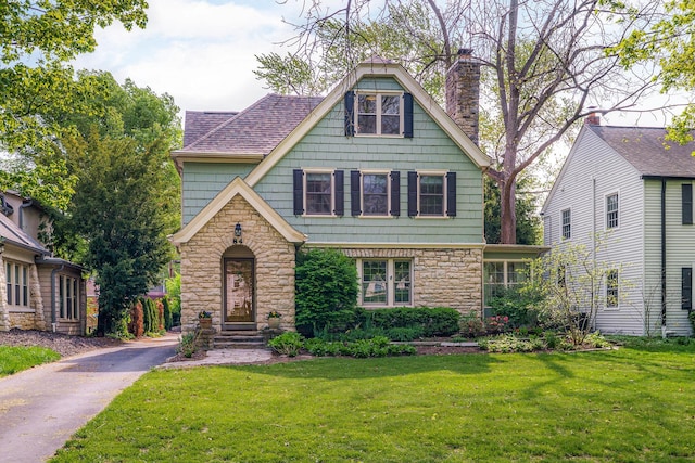 tudor house featuring a front yard, a chimney, and stone siding