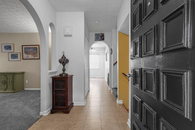 5968 Lisa St, Columbus, OH 43231 - hallway featuring arched walkways, a textured ceiling, light tile patterned floors, baseboards, and light carpet