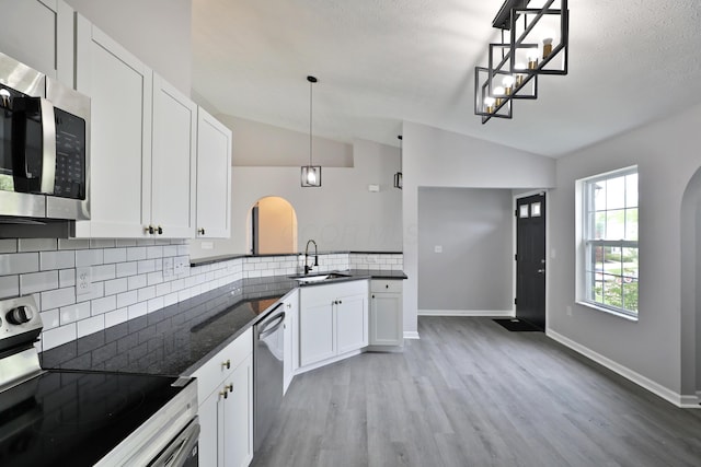 kitchen featuring a sink, arched walkways, light wood-style flooring, stainless steel appliances, and lofted ceiling