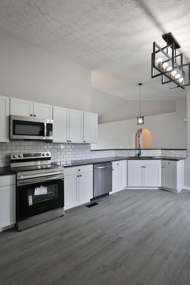 kitchen with appliances with stainless steel finishes, tasteful backsplash, dark countertops, a sink, and dark wood-style floors