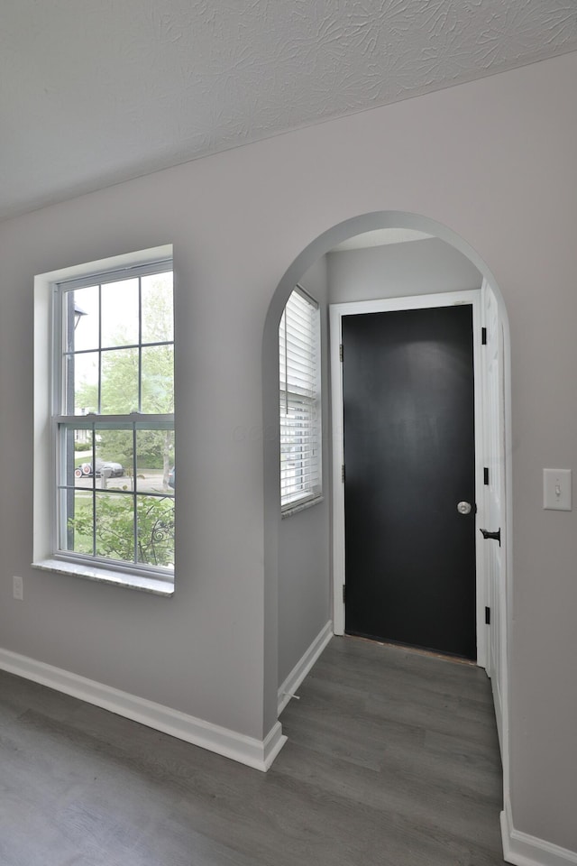entrance foyer featuring baseboards, arched walkways, and wood finished floors