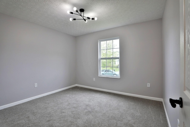 carpeted spare room featuring an inviting chandelier, a textured ceiling, and baseboards