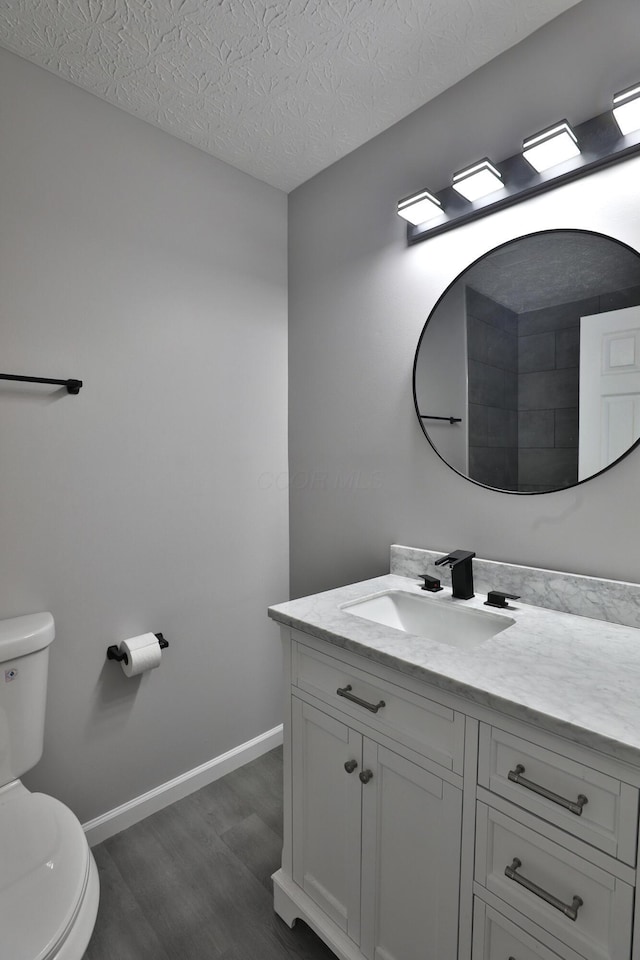bathroom with vanity, toilet, a textured ceiling, baseboards, and wood finished floors